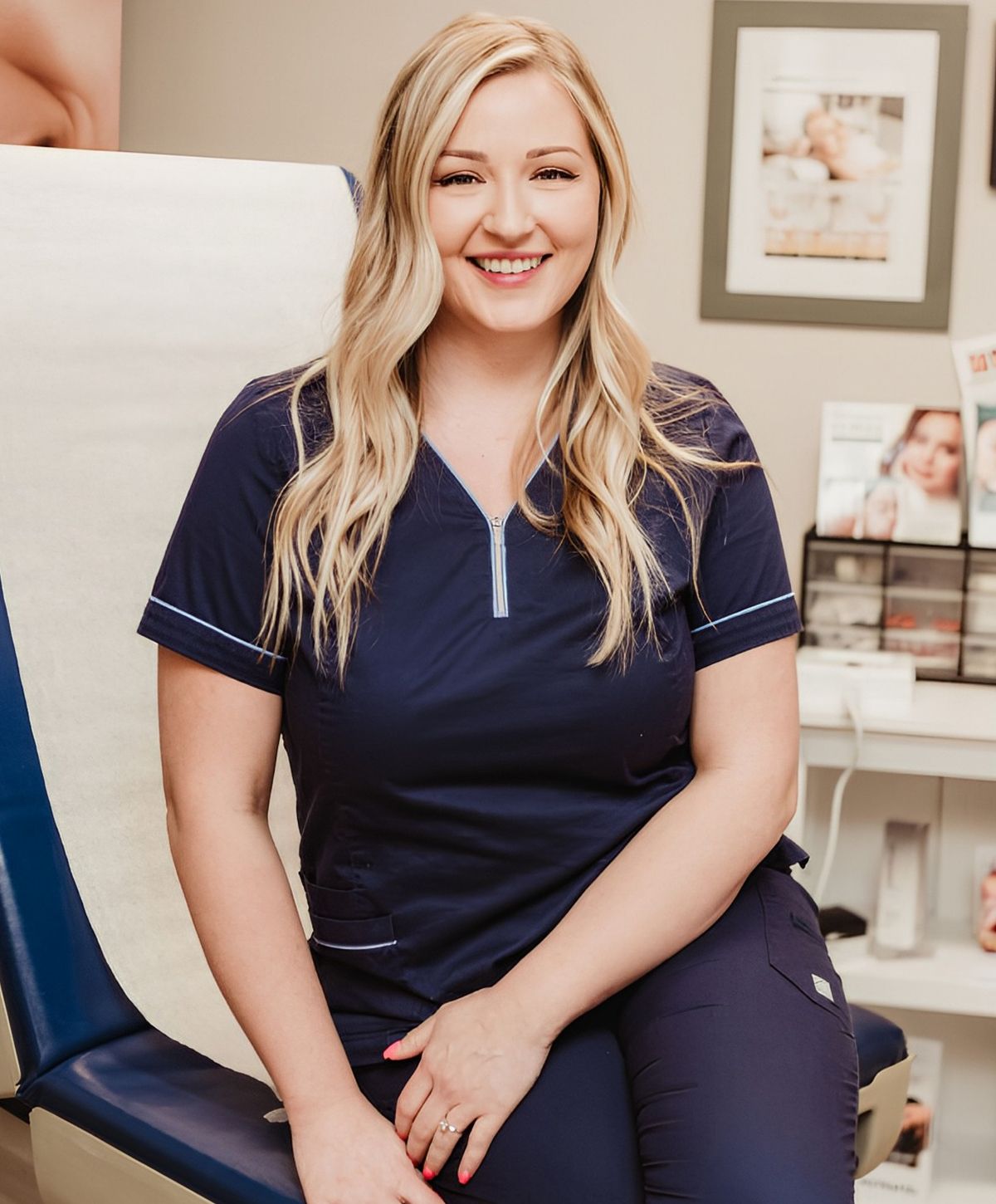 Smiling woman in medical scrubs, seated in clinic.