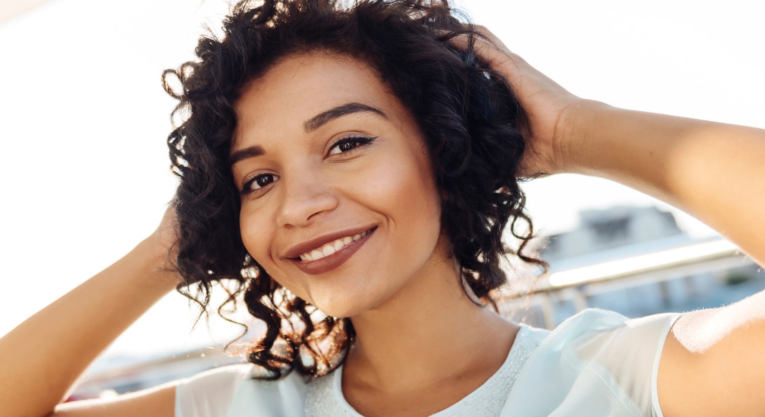 Smiling woman with curly hair outdoors.