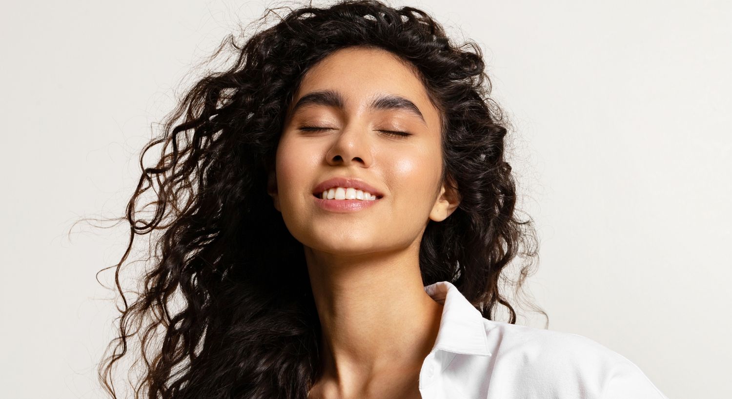 Woman with curly hair smiling and eyes closed.