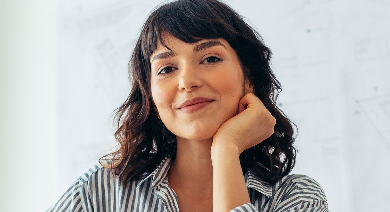 Woman smiling with hand on chin, professional setting.
