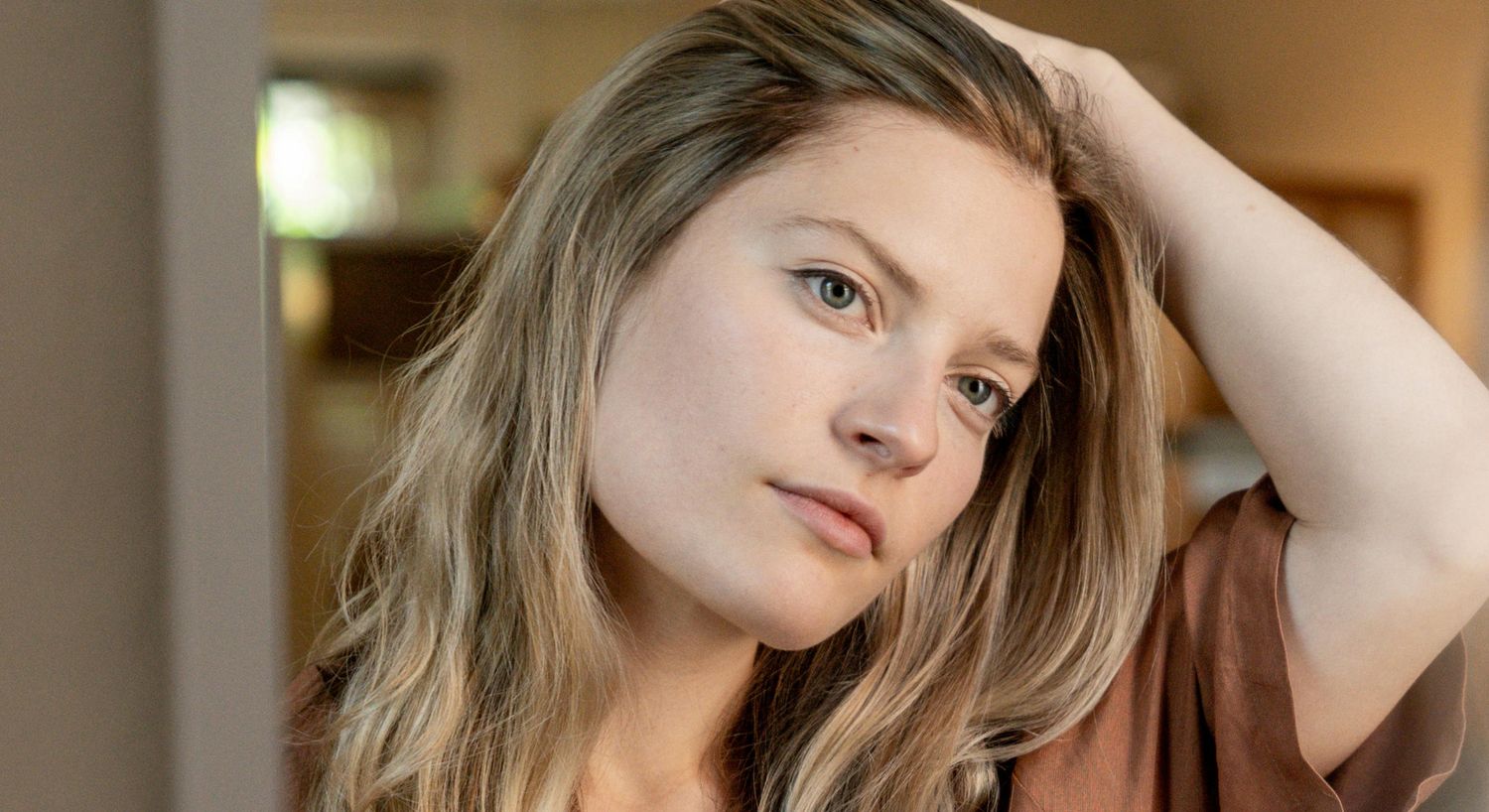 Person with long hair looking thoughtfully at camera.