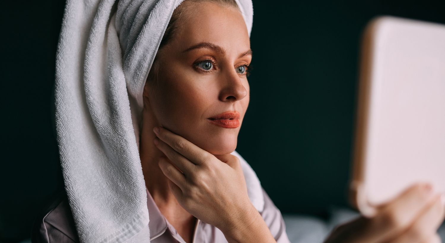 Woman with towel looking at mirror reflection.
