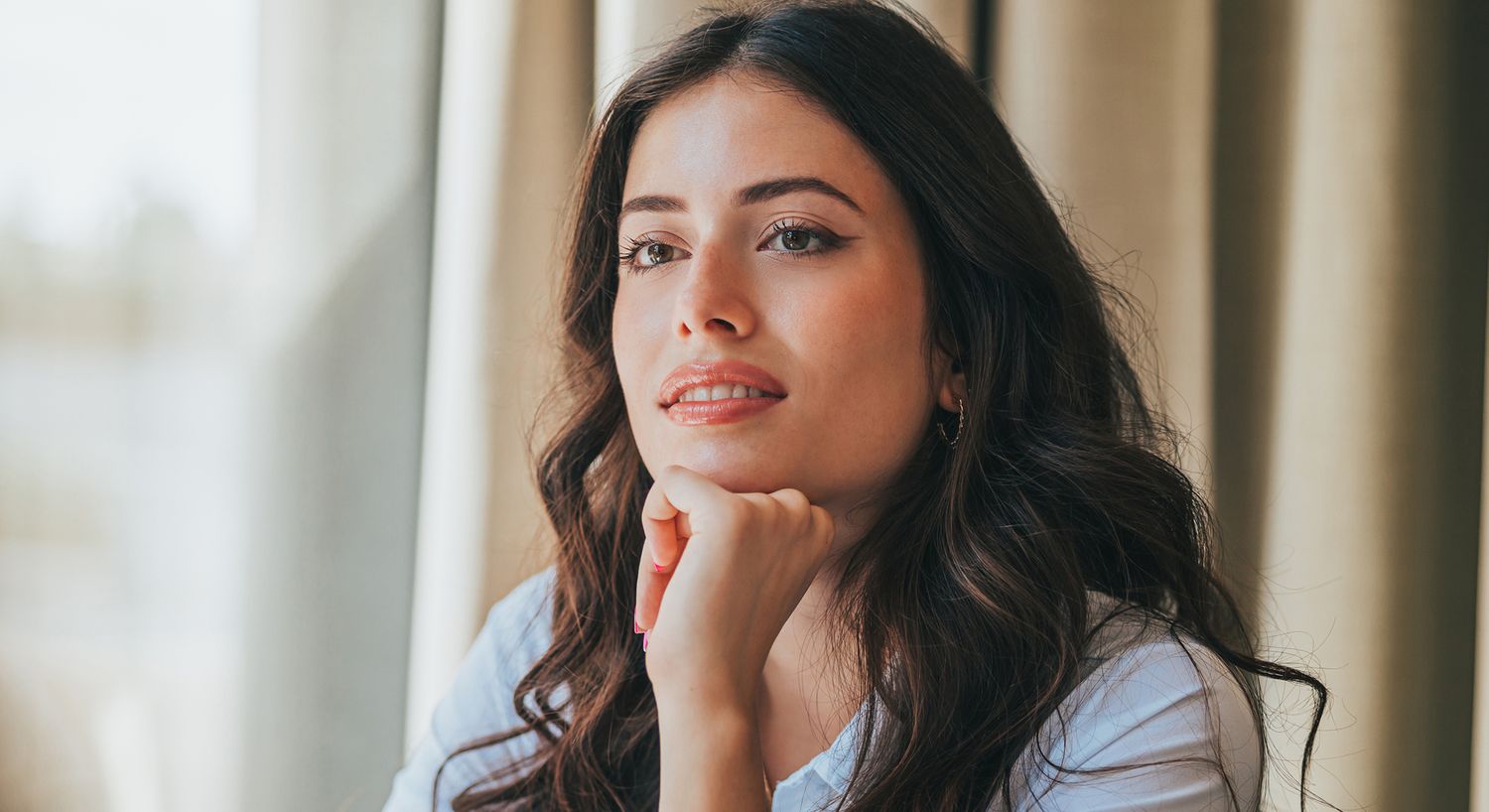 Thoughtful young woman resting her chin on hand.